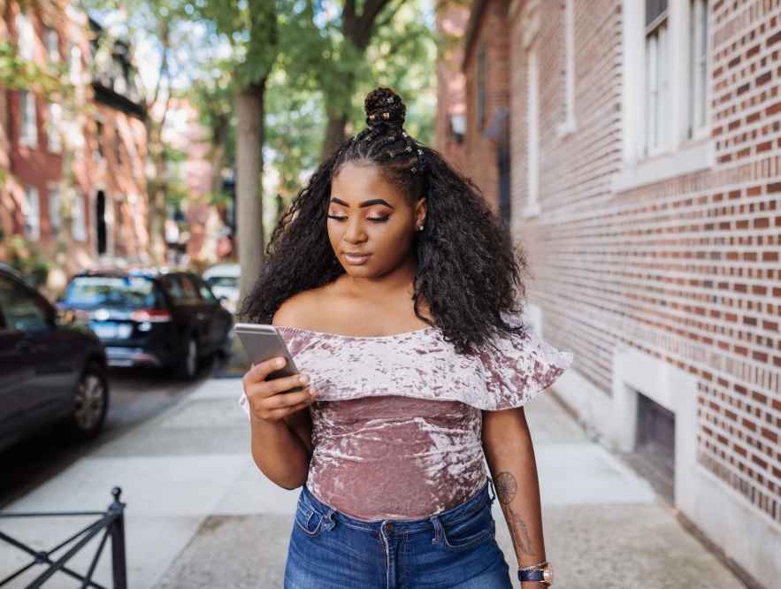 A young black woman walking outside and looking at her phone